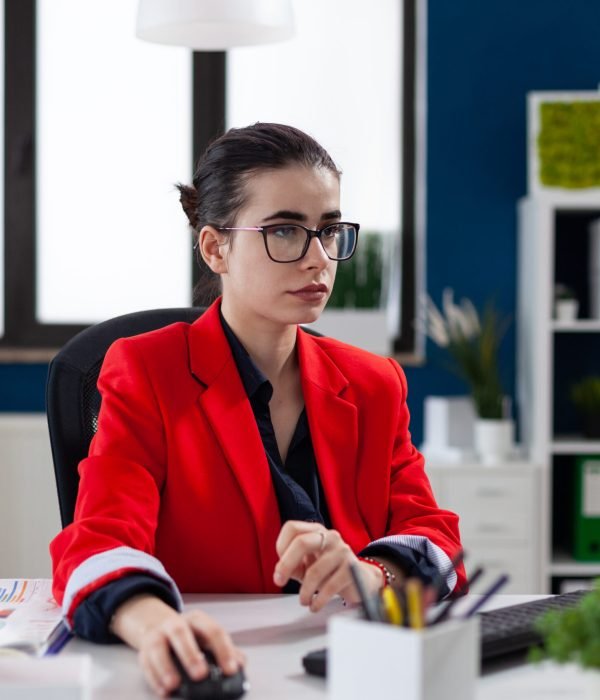 Focused businesswoman in corporate office workplace, working on computer, making financial analysis. Concentrated entrepreneur using mouse with wireles technology sitting at desk.